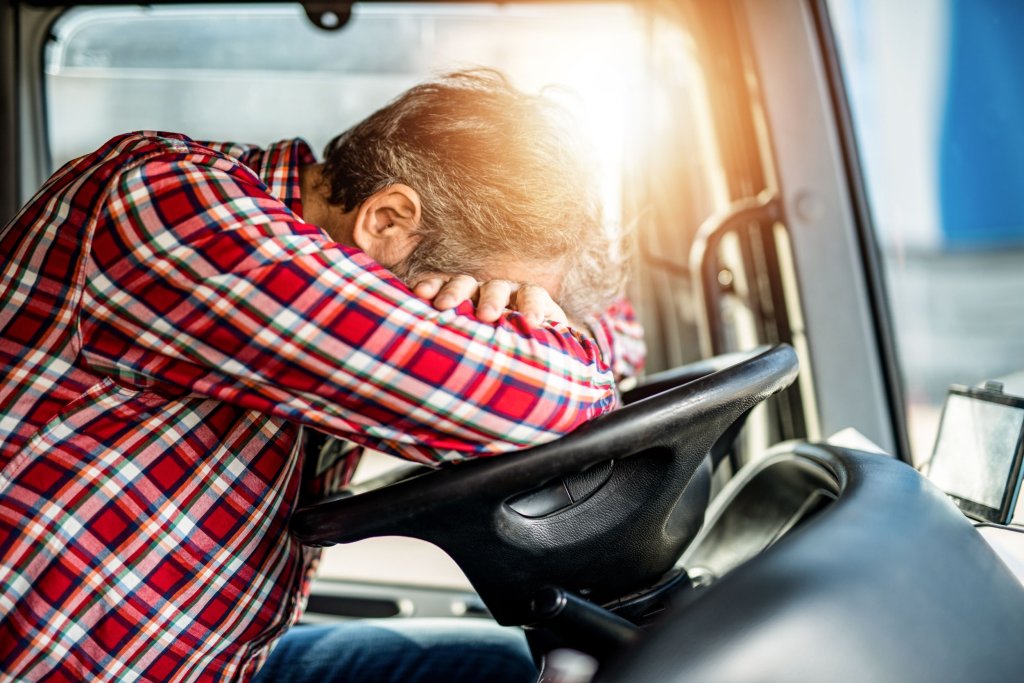 A trucker laying with his head and arms crossed on the wheel